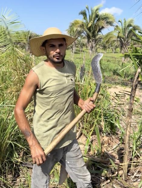 Reinaldo da Silva Melo, also known as the "King of Juquira", holding a scythe while standing in a field.