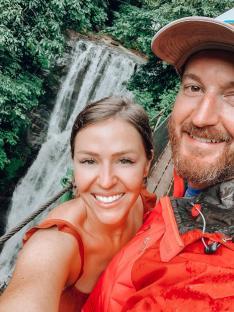 Couple posing for a selfie in front of a waterfall.