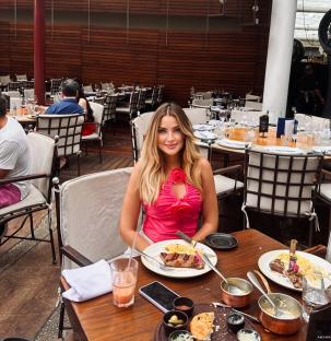 Woman sitting at an outdoor restaurant table eating a steak.