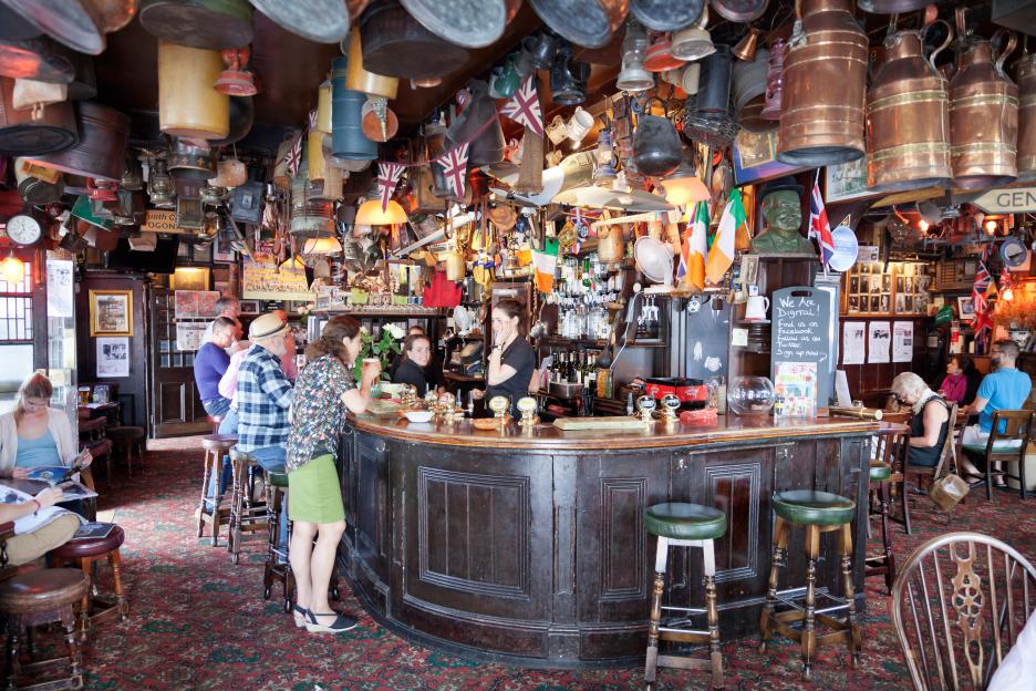 People at the Churchill Arms Pub in Kensington, London, known for its elaborate interior decor with hanging items and flags.
