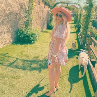 Woman in a pink dress and hat walking two dogs on a grassy path.
