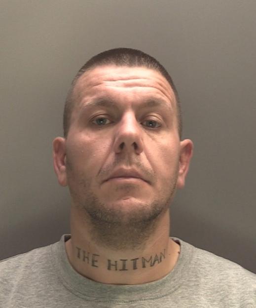 Mugshot of a man with "The Hitman" tattooed on his neck.