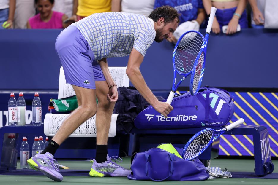 Daniil Medvedev putting his broken tennis racket into his bag after losing a match.