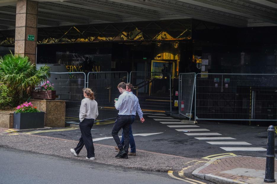 Three people walking past a Britannia Hotel entrance blocked by a temporary fence.