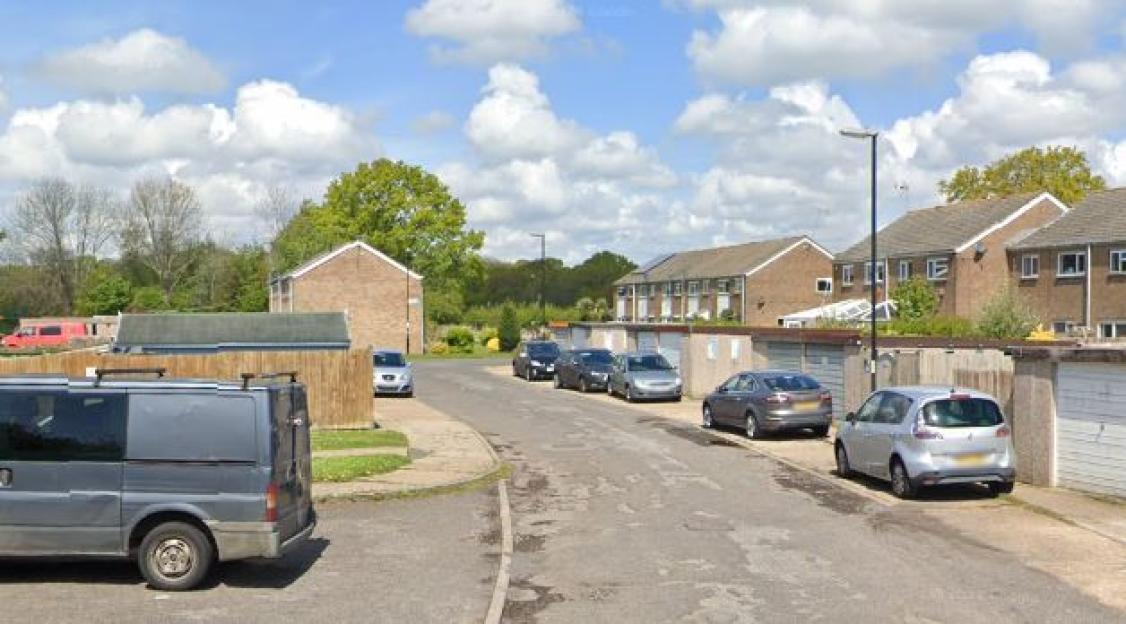 Residential street with parked cars and garages lining the road.