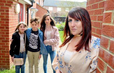 A woman with her three grandchildren outside a brick building.