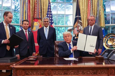 President Trump signing executive orders in the Oval Office with White House staff.