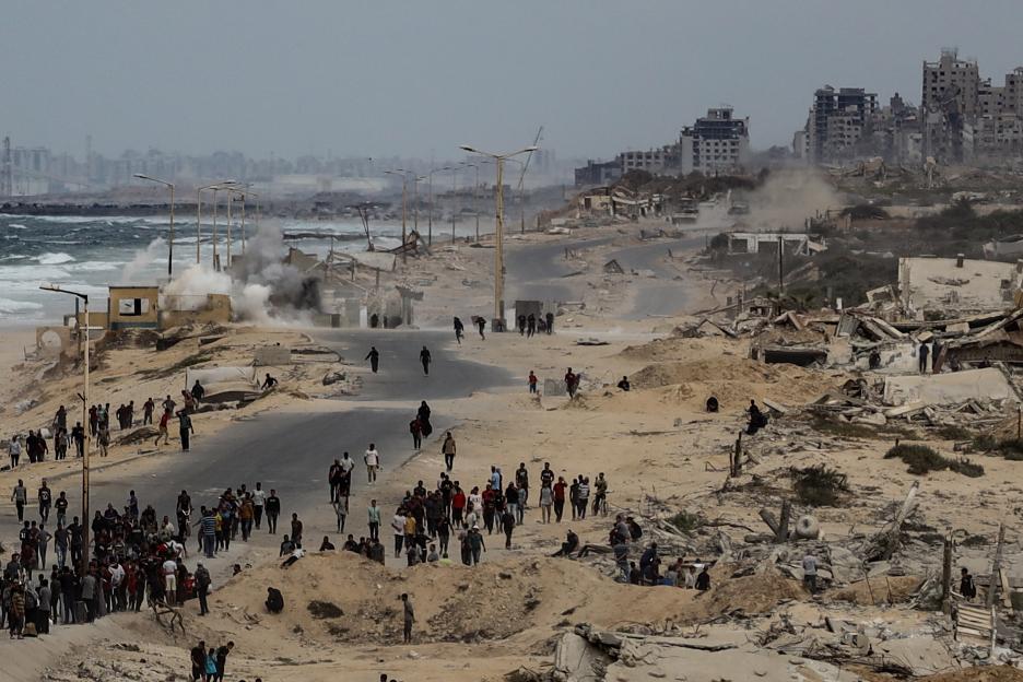 People on Rashid Street in Deir al-Balah, Gaza, amid smoke from an attack and surrounding destroyed buildings.