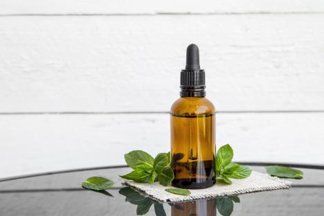 Amber bottle of peppermint essential oil with fresh mint leaves.