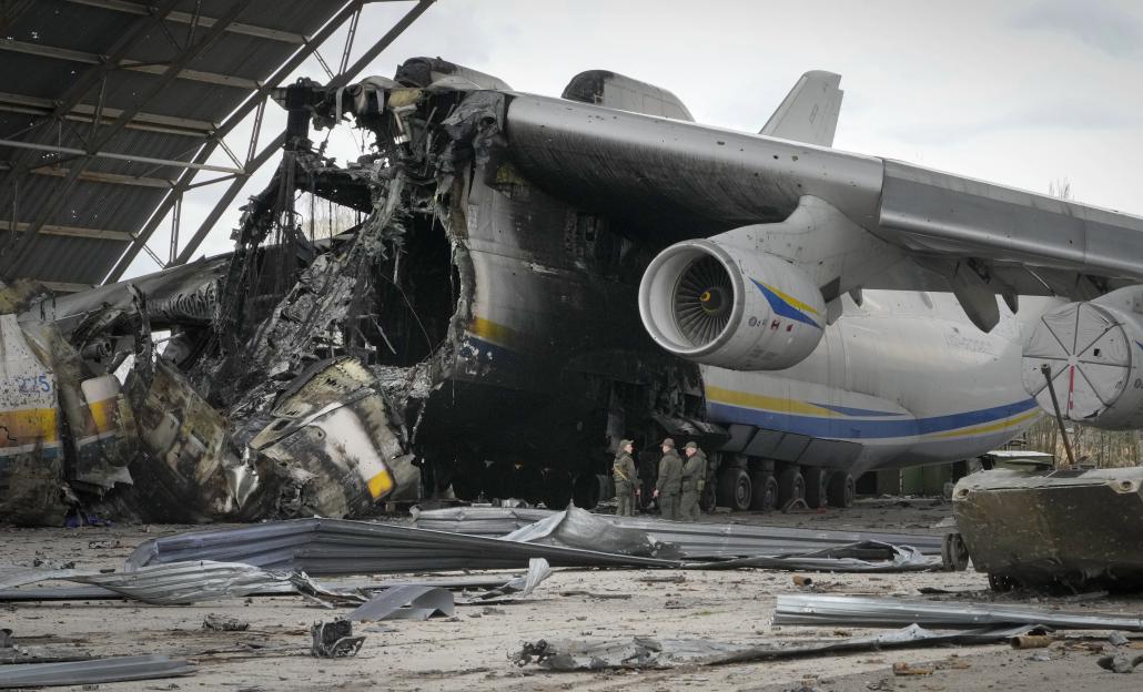 Three Ukrainian soldiers stand by the remains of the destroyed Antonov An-225 cargo aircraft in a hangar.