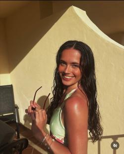 Woman with long dark hair smiling, holding sunglasses.