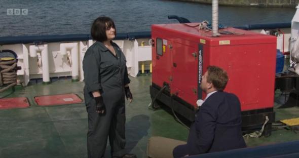 A woman in a dark green jumpsuit confronts a man in a suit on the deck of a ship, near a red generator.