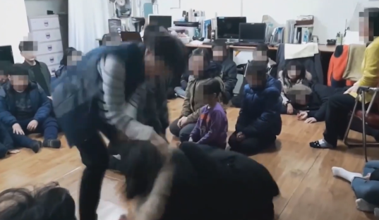 A person interacting with a group of children sitting on the floor.