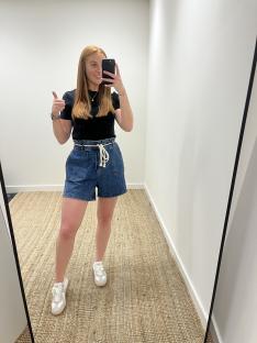Woman giving thumbs up while wearing denim shorts and sneakers.