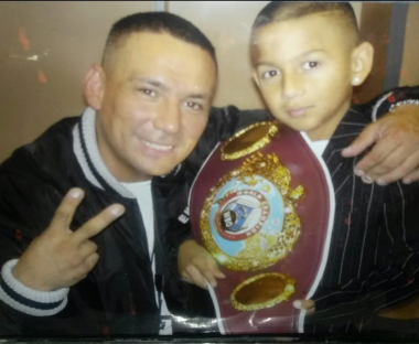 A man and a young boy pose with a boxing championship belt.