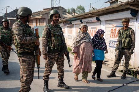 Indian security forces standing guard as a woman and girl walk past.