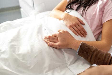 Close-up of a person holding the hand of a person lying in a hospital bed.