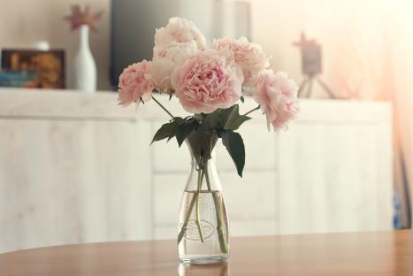 Pink peonies in a glass vase on a wooden table.