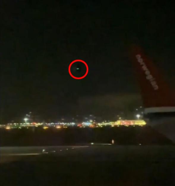 Green light circled in red in the night sky.