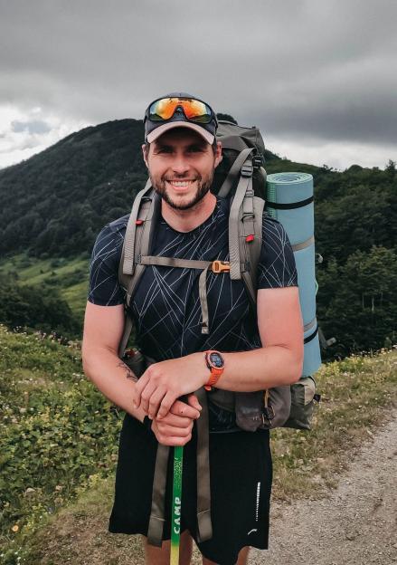 A smiling hiker with a backpack and trekking poles.