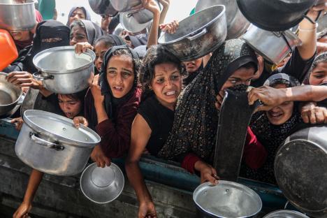 Palestinian women and children holding pots and bowls during a food distribution in Khan Yunis, Gaza.