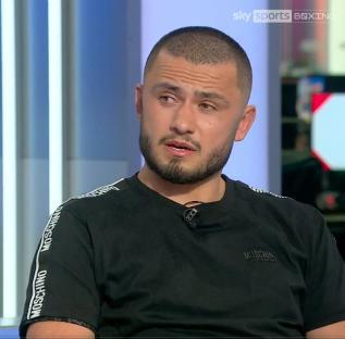 A man in a black Moschino t-shirt sits for an interview.