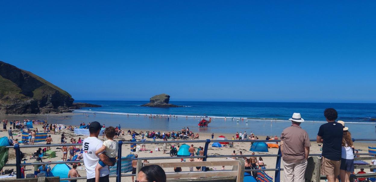 Crowded beach with a helicopter landing on the sand.