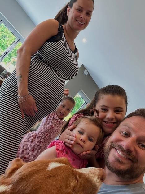 Family photo of pregnant mother, father, three daughters, and dog.