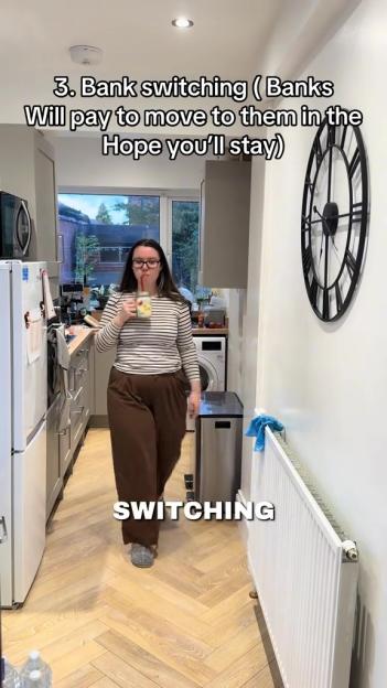 A woman in a striped shirt and brown pants walks through a kitchen, drinking from a glass, with text overlaid: "3. Bank switching (Banks Will pay to move to them in the Hope you'll stay) SWITCHING".