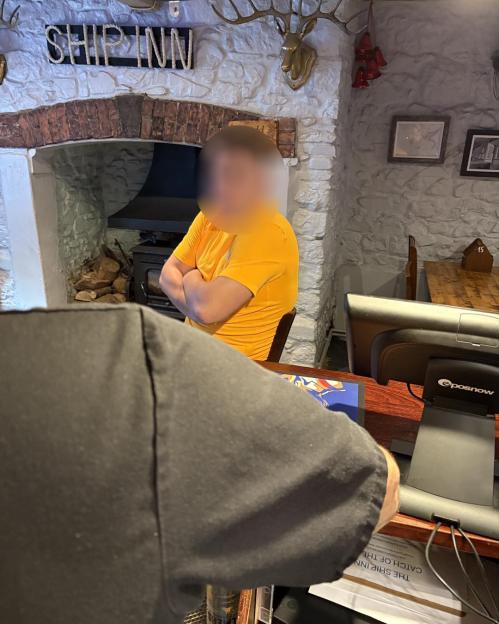 Photo of a man in a yellow shirt at a pub counter, his face blurred.