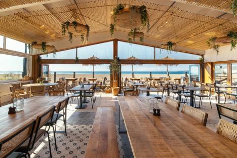 Beachfront restaurant with large wooden tables and ocean view.