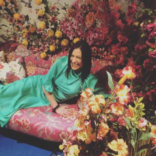 Woman in teal dress smiling on floral couch.