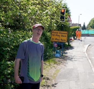 A man stands near a road closure sign during HS2 construction.