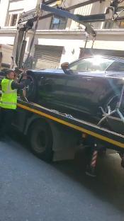 A dark-colored sports car being towed away on a flatbed truck.