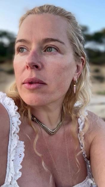 Amanda de Cadenet in a white top with multiple necklaces and earrings, looking left.