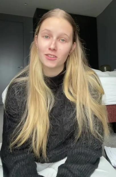 A young woman with long blonde hair and a black sweater talks to the camera.