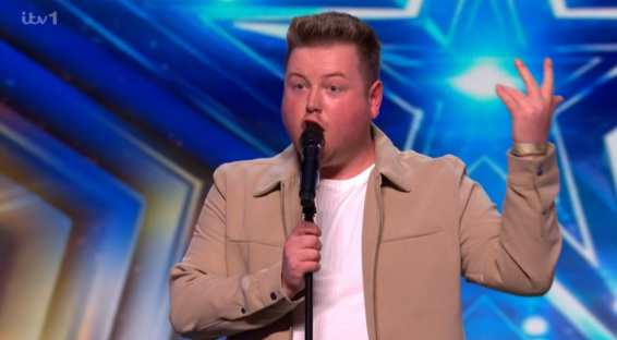 Screenshot of a man singing into a microphone on a stage.
