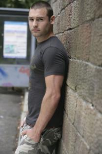 Russ from Hollyoaks leaning against a brick wall.