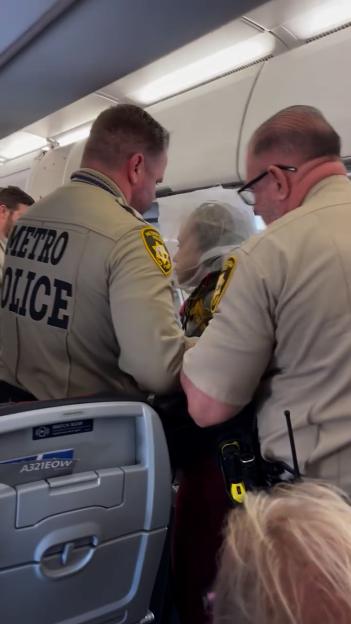 Two Metro Police officers escorting a passenger with a spit hood on an airplane.