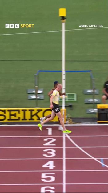 A runner helping another runner cross the finish line of a 3000m steeplechase.