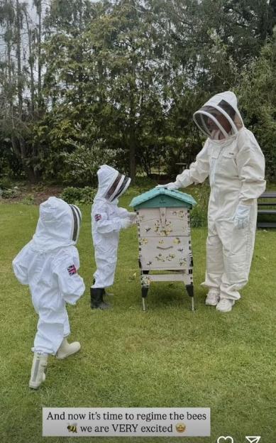 A person and two children in beekeeping suits tending to a beehive.