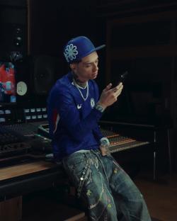 A person wearing a Chelsea football jersey uses a smartphone in a recording studio.
