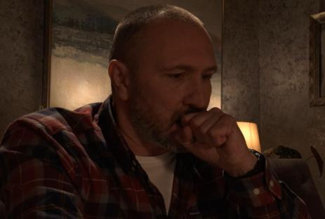 Man in plaid shirt coughs into his hand.