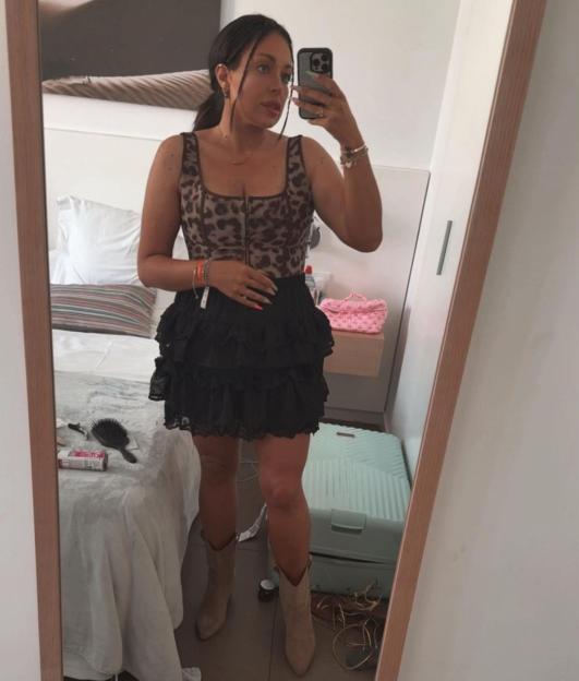 Mirror selfie of a person wearing a leopard print top and layered black skirt with cowboy boots.