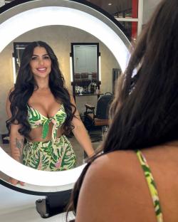 Woman looking at her reflection in a lighted mirror, wearing a tropical-print two-piece outfit.