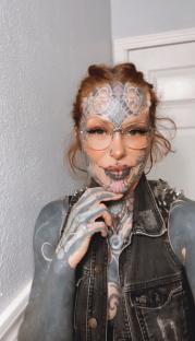 Portrait of a heavily tattooed woman wearing glasses and a denim vest.