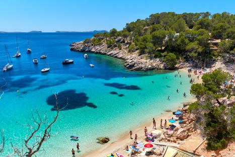 Cala Salada lagoon in Ibiza, Spain, with boats and people enjoying the beach.