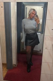 Mirror selfie of a woman in a grey top and black skirt.
