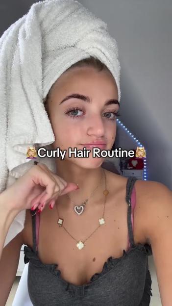 Woman with towel-dried hair demonstrating a curly hair routine.