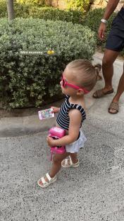 Toddler girl wearing sunglasses and holding toy phone and camera.